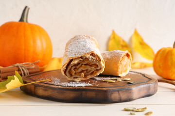 Board with tasty pumpkin strudel, seeds and cinnamon on white wooden table