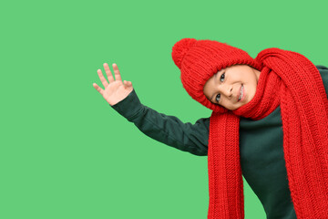 Cute little Asian boy in red knitted hat and scarf on green background