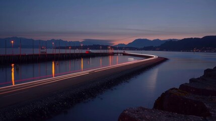 Obraz premium The calm waters of the harbor reflect the glowing car light trails creating a serene and picturesque view.