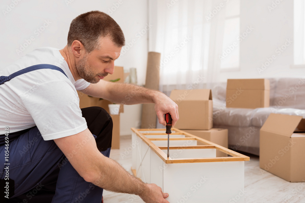 Aufkleber Professional Furniture Assembler Man Fixing And Assembling Wooden Shelf After Relocation Sitting On Floor Indoors. Side View Of Carpenter Working Using Screwdriver Tool. Carpentry Service Concept