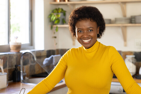 Smiling African american woman in yellow sweater enjoying time in cozy kitchen at home