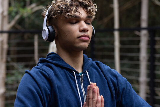 Young man meditating on balcony wearing headphones, finding peace and relaxation