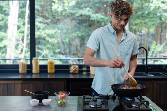 Young man cooking in modern kitchen, stirring vegetables in frying pan, at home