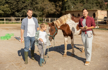 Boy with young man and woman leads horse on tether in paddock