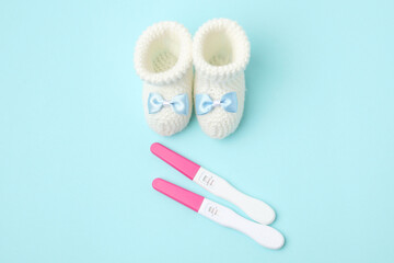 Pregnancy tests and knitted booties on light blue background, top view