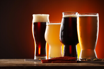 Glasses with different types of beer and snacks on wooden table against color background