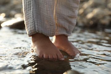 Cute little girl standing in water outdoors, closeup. Child enjoying beautiful nature