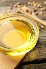 Cooking oil in bowl and soybeans on wooden table, closeup
