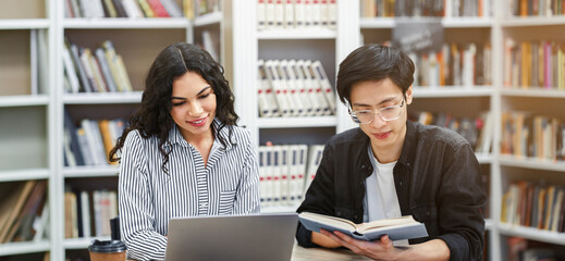 Preparing For Seminar. Two multiethnic students studying together sitting at desk in campus library