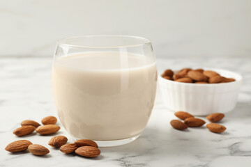 Glass of almond milk and nuts on white marble table, closeup