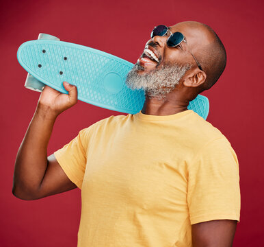 Laughing, skateboard and sunglasses with mature black man on red background isolated in studio. Action, active or funny and happy African person having fun with skating or sports for wellness