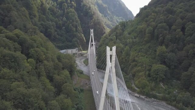Aerial around epic modern cable-stayed bridge Adler road Krasnaya polyana Sochi Russia suburban freeway cars traffic among high mountains. Natural landscape green slopes. Travel landmark. High quality