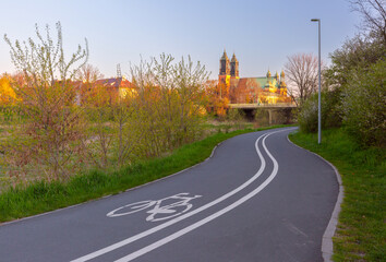 A bicycle path winding through greenery with a view of the Cathedral Basilica of St. Peter and St. Paul in the background at sunrise in Poznan, Poland