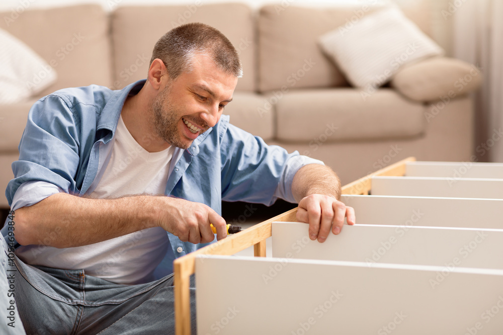 Poster smiling man assembling furniture installing cabinet after relocation sitting at home. selective focu