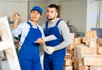 Caucasian man and asian woman builders discussing project documentation in apartment. Pointing...