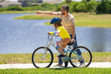 Obraz premium Father support son. Sporty family father and son riding bike on a park. Child in safety helmet riding bike on summer day. Father teaching son riding on bike. Child son in bike helmet on bicycle