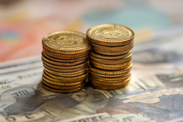 A stack of gold coins on top of a stack of bills. The coins are of different sizes and colors