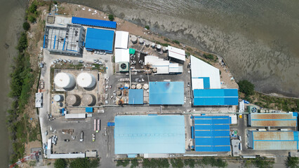 A busy factory with large tanks and trucks loading and unloading. The industrial activity is constant, with vehicles moving between towering storage units.