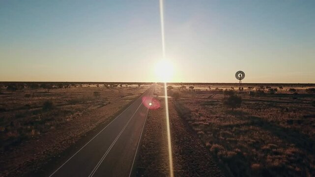 Aerial view. Silhouette of a large windmill in central Australia rotating in slow motion against dramatic Australian outback sunset. No people. Red center Uluru