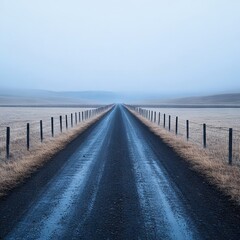 Fototapeta premium A long, empty road stretches through a misty landscape, evoking solitude.
