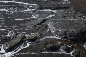 Foamy sea water on large black stones. Space for text. Background. Close-up.