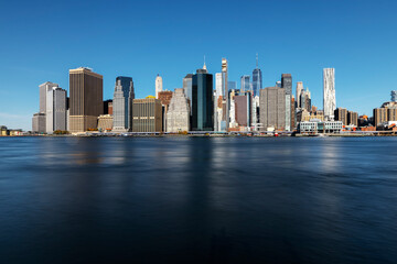 Naklejka premium Downtown Manhattan Skyline : A stunning view showcasing iconic skyscrapers and the historic bridge, beautifully illuminated at sunset, reflecting the vibrant energy of New York City