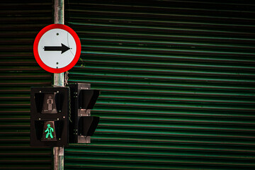 green go pedestrian traffic light and one-way traffic sign with green iron door on the street in...