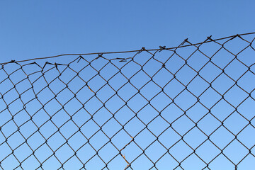 Damaged chain-link fence against a clear blue sky background