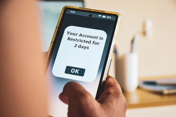 Man holding phone showing account restricted message for two days. Selective focus. Social media account restrictions concept. 