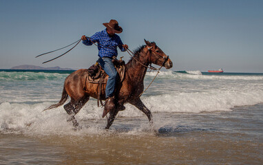 A cowboy riding a horse in the water causing splashes at a beach. The image is from Rosarito Mexico