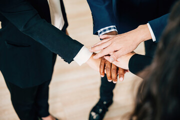 Colleagues from various ethnicities and backgrounds join hands in a modern office, emphasizing teamwork, cooperation, and community. An above view showcases their commitment to equality and diversity.