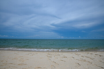 Sunny tropical beach with ocean waves, blue sky, and clouds on the horizon