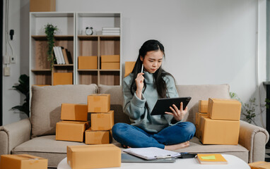 woman using smartphone or tablet taking receive and checking online purchase shopping order to preparing pack product box. .