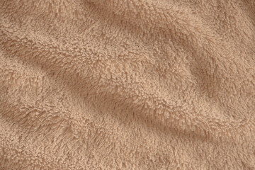 Beige delicate soft background of plush fabric. Texture of soft faux fur blanket textile with beautiful folds, close-up, high resolution.