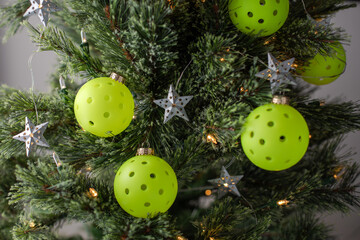 Close view of a Christmas tree decorated with pickleballs as ornaments and shining lights and stars. Selective focus. Pickleball Christmas tree backdrop.