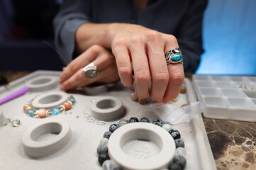 Caucasian woman assembles handmade jewelry bracelets made of stones and metal in her workshop with dark lighting and mysterious atmosphere