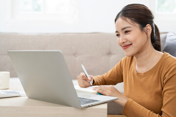 Happy smiling middle aged woman using laptop computer sitting at table in living room