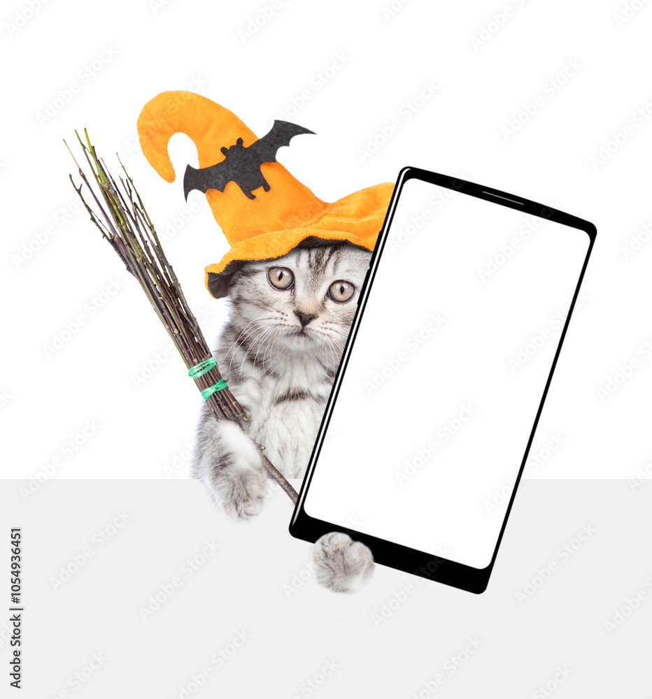 Poster cute kitten wearing hat for halloween holds shows smartphone with white blank screen in it paw above