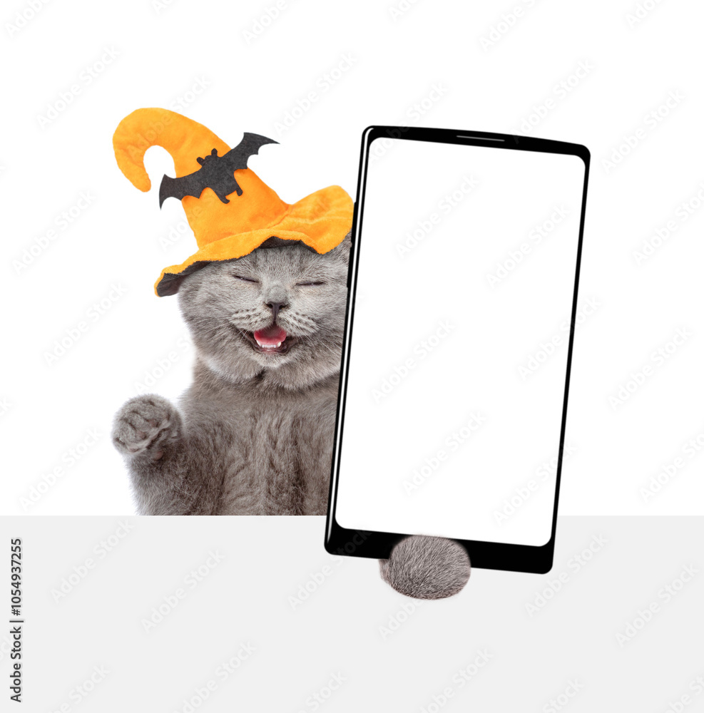 Poster happy kitten wearing hat for halloween holds shows smartphone with white blank screen in it paw abov