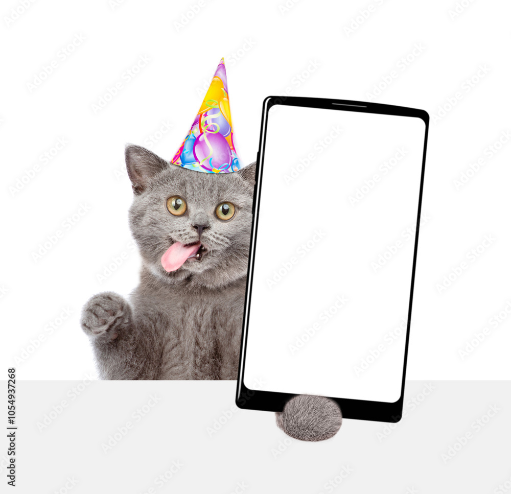Poster Happy kitten with tongue out wearing party cap shows big smartphone with blank screen above empty white banner. Empty space for text. isolated on white background