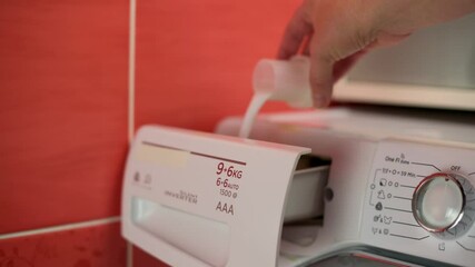 Close-up of hand pouring liquid detergent into detergent compartment of washing machine in tiled laundry room. Woman hand pouring liquid detergent into detergent compartment. Hand pouring liquid  - Powered by Adobe