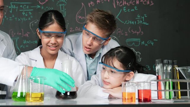 Girl looking at beaker while doing experiment at blackboard with chemistry theory in STEM class. teacher and group of high school student with mixed races doing science activity together. Edification