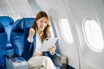 Asian female passenger of airplane sitting in comfortable seat while working laptop and tablet. Travel in style,