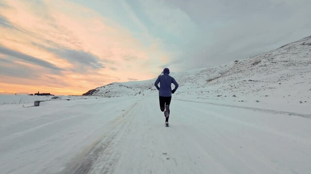Aerial drone view of young man jogging outdoors with snowy mountains in the background. Healthy running and exercise concept outdoors, high-speed drone fvp shooting, slow motion