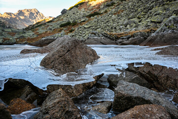 Ice sheet forming over a mountain lake in the tatra mountains, with rocks and mountains in the background