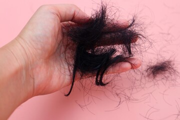 Hair loss or alopecia on woman's hand close up. With a pink background.
