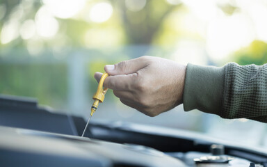 Car owner pulls out the dipstick to check engine oil levels, highlighting the importance of regular oil maintenance for optimal engine performance and vehicle longevity