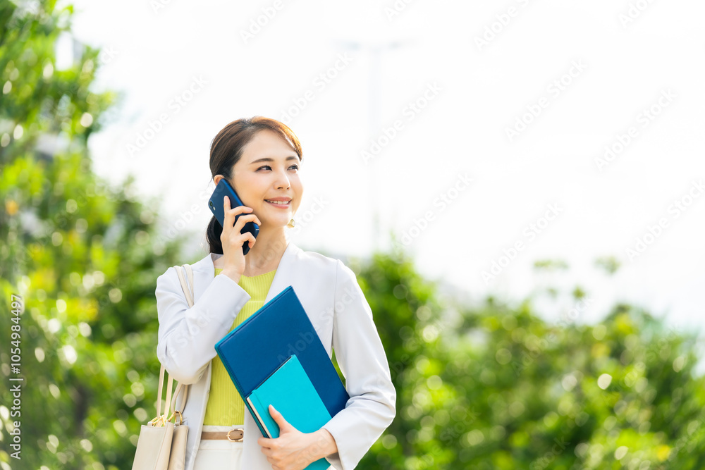 Leinwandbilder 通話、女性、ビジネス、ビジネスウーマン、キャリアウーマン、電話、スマートフォン、スマホ、日本人、屋外、歩く、OL、仕事、会社員、営業、サラリーマン、街路樹、緑、グリーン、環境、若い、20代、30代、働く、笑顔、ポジティブ、やる気、通信、連絡、報告、問い合わせ、訪問、通勤、出張、アウトドア、爽やか、美人、明るい、書類、ビジネスパーソン、元気、経営、マネジメント、人材、空、コピースペース、スーツ、携帯
