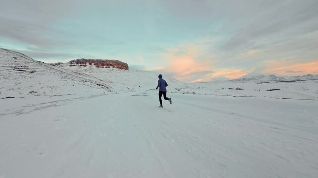 Aerial drone view of young man jogging outdoors with snowy mountains in the background. Healthy running and exercise concept outdoors, high-speed drone fvp shooting, slow motion