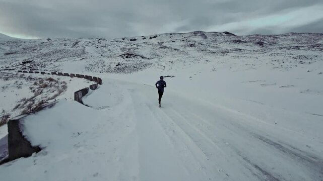 Aerial drone view of young man jogging outdoors with snowy mountains in the background. Healthy running and exercise concept outdoors, high-speed drone fvp shooting, slow motion